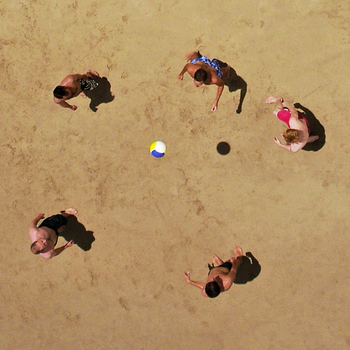Aerial photograph of five people standing on sand around a ball.