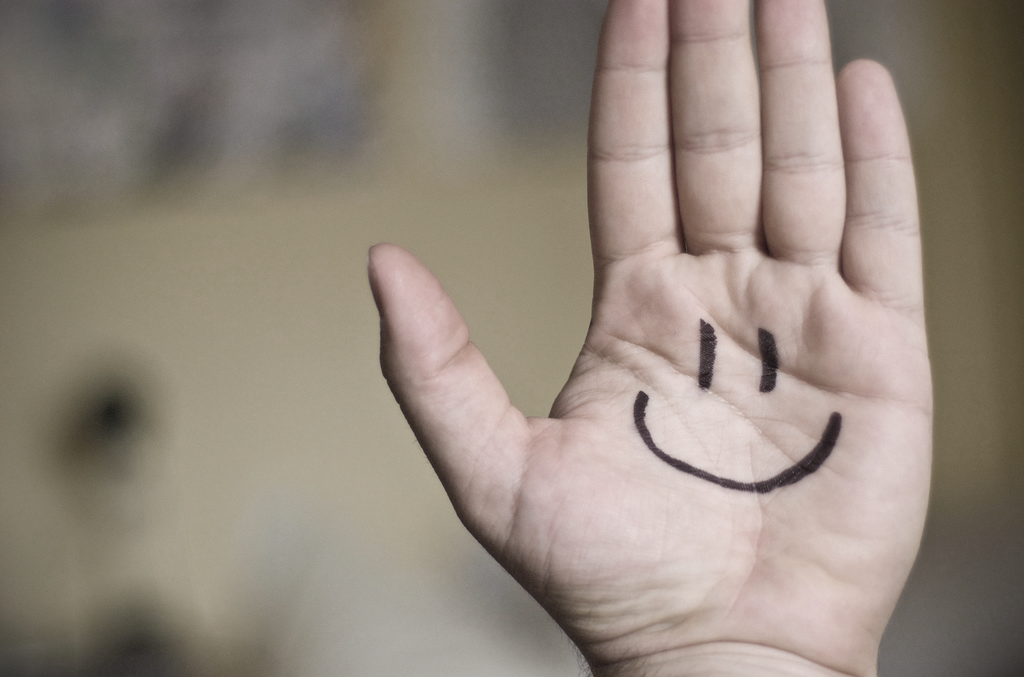 An open palm has a smiling face drawn on it.