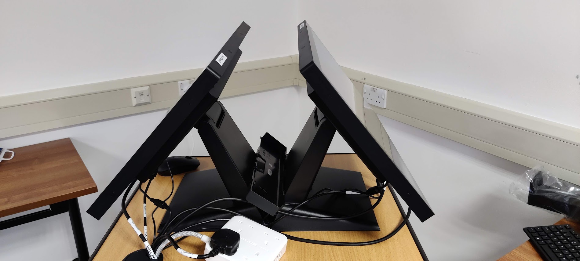 Photograph of two large monitors standing in a V shape on a wooden desk, with cables running behind them.