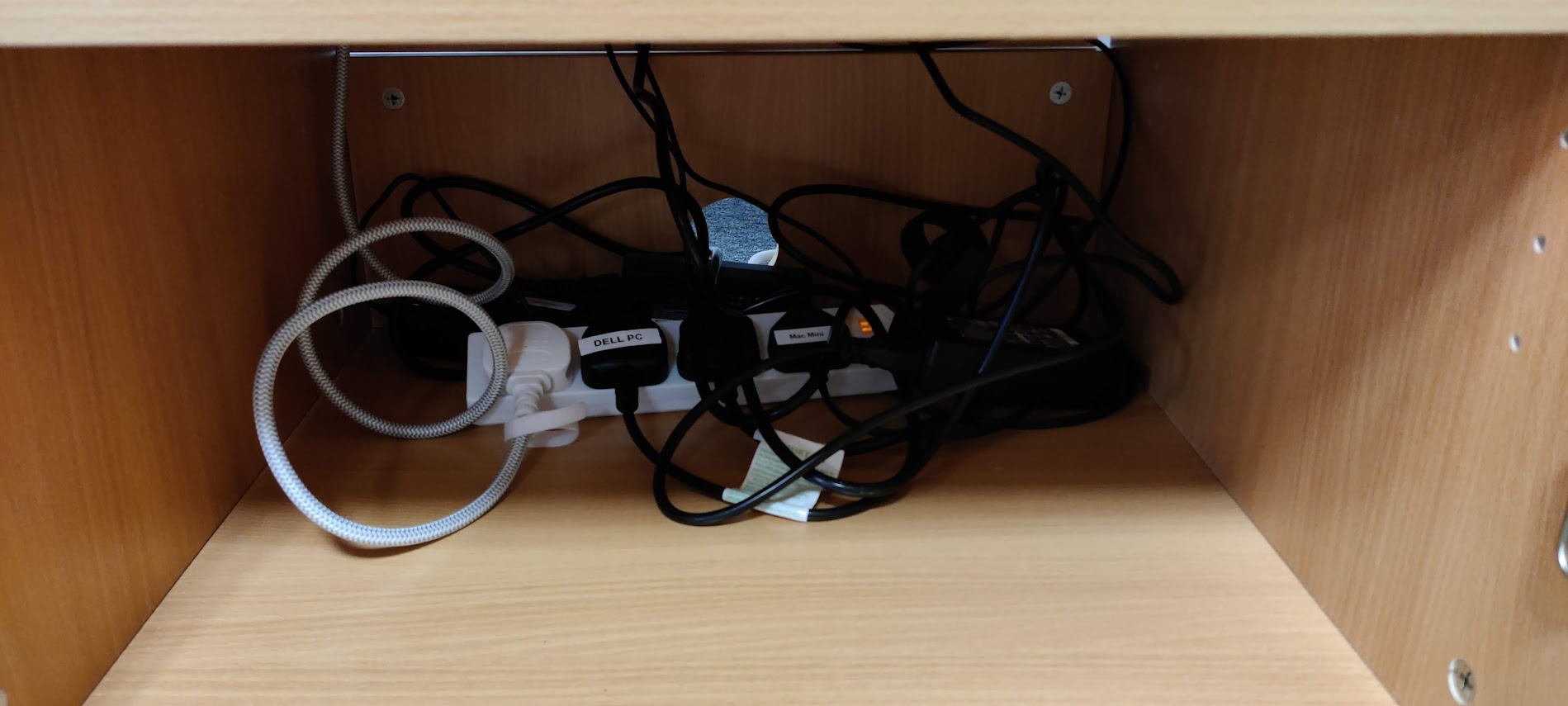Photograph of tangled power and data cables and a power strip inside a wooden cabinet.