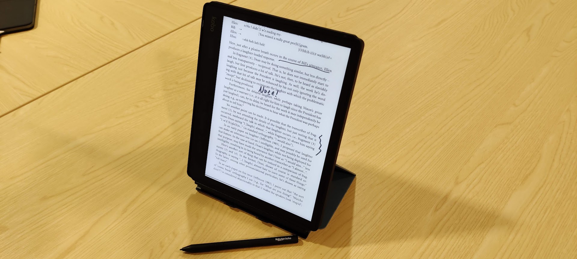 Photograph of a Kobo e-reader standing upright on a stand, showing handwritten notes on a page.