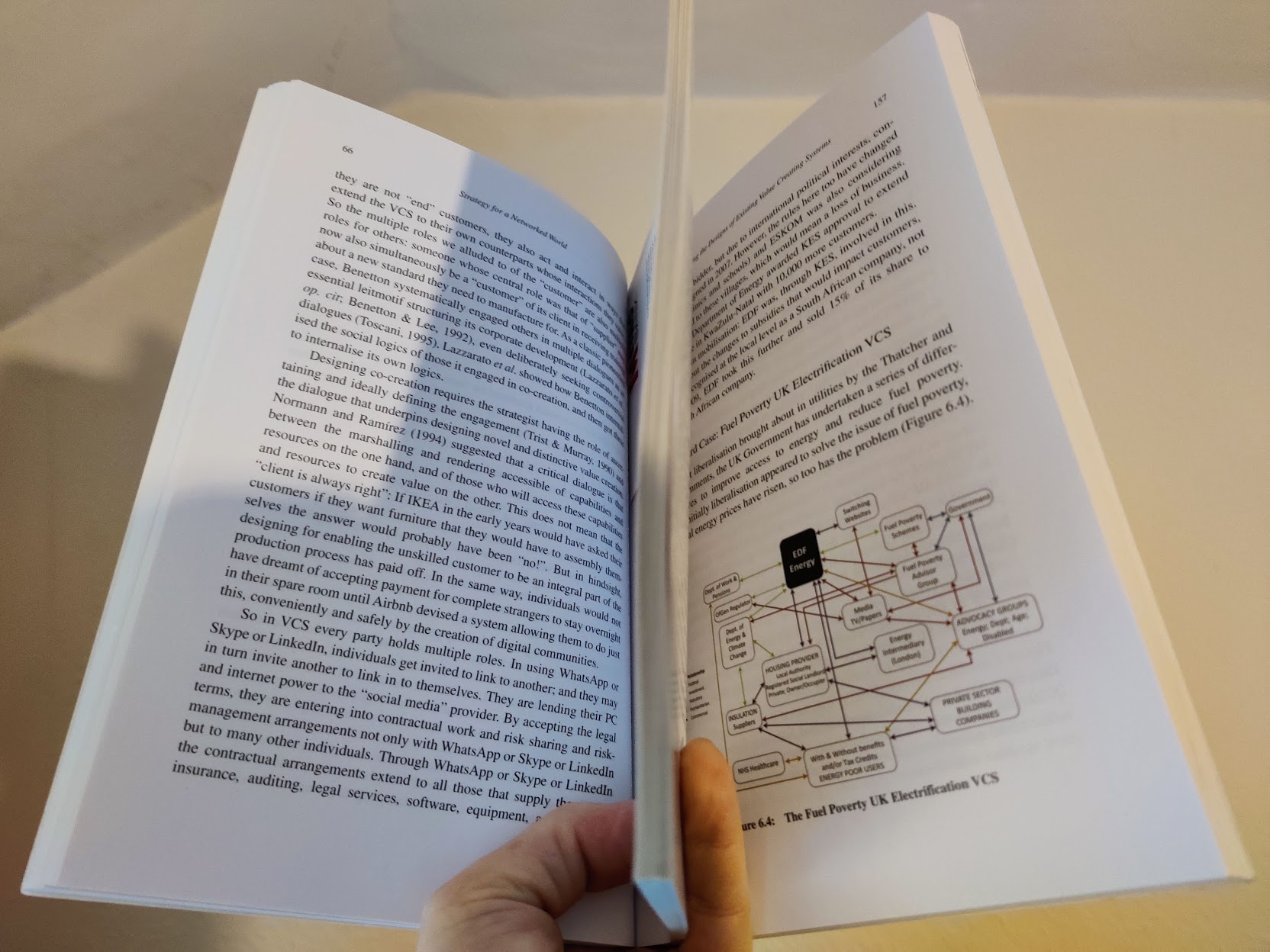 Photograph of hands holding a thick printed book open, with a diagram in the text and a thumb marking a page.
