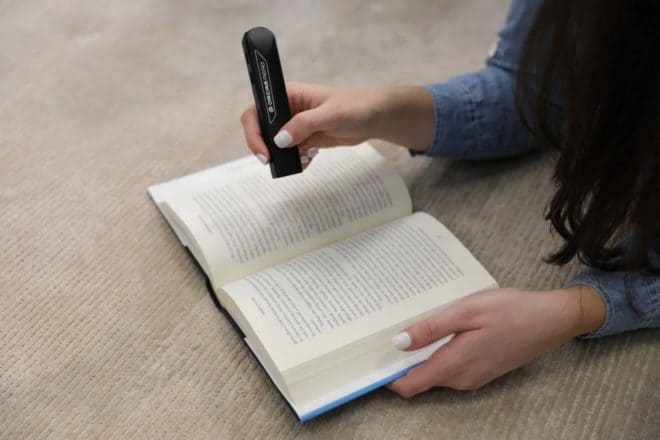 Photograph of a woman holding a pen-shaped reader above an open book.