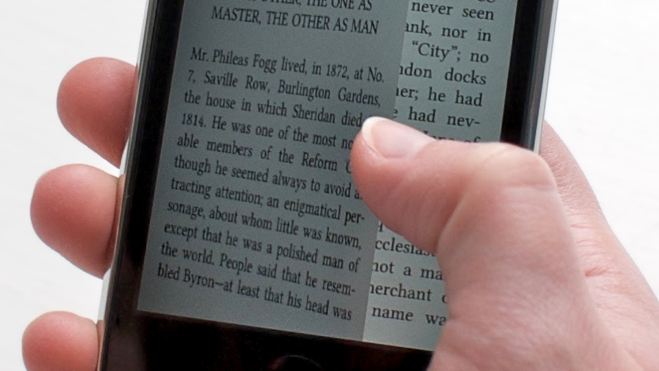 A close-up photograph of a hand holding a phone whose screen shows a page of book text.