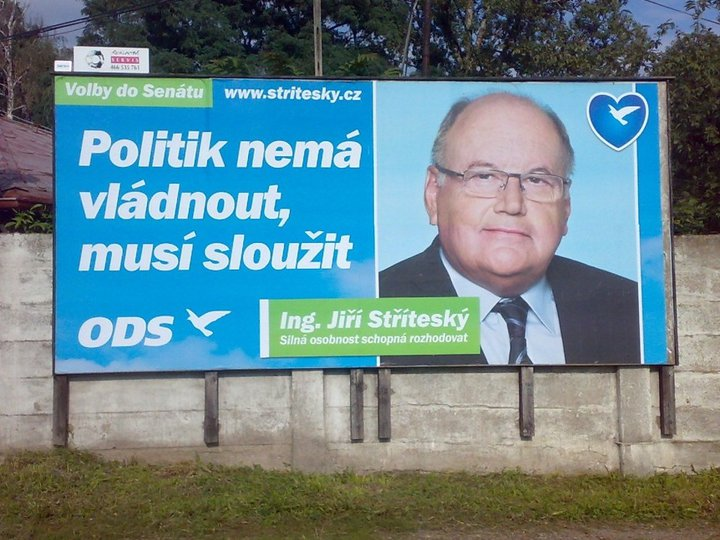 Photograph of a blue billboard on a concrete wall with the text “Volby do Senátu”, “Politik nemá vládnout, musí sloužit”, the ODS logo, a web address, and a portrait of an older man with glasses and a caption naming him with the phrase “Silná osobnost schopná rozhodovat”.