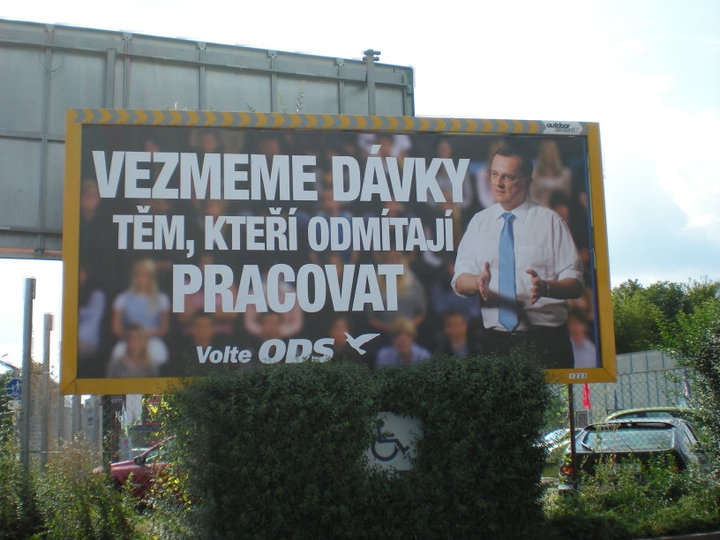 Photograph of a yellow-framed billboard showing a man in a blue tie gesturing before a crowd, with the text “Vezmeme dávky těm, kteří odmítají pracovat” and “Volte ODS”.