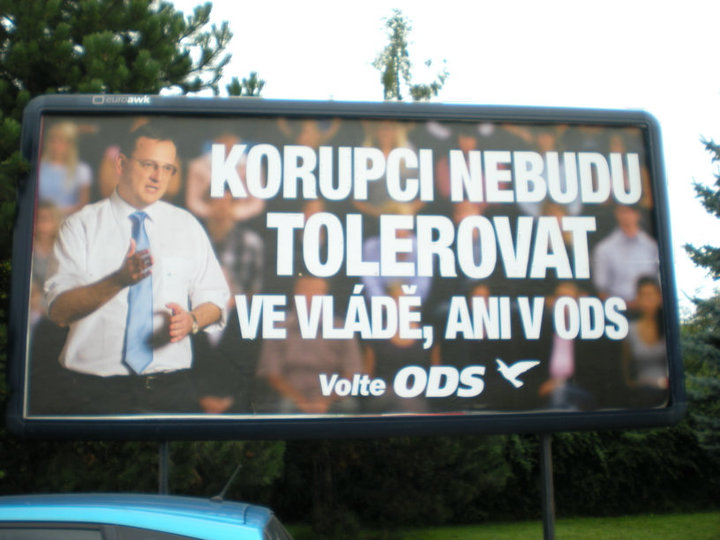 Photograph of a dark billboard showing a man in a white shirt and tie gesturing before a blurred crowd, with the text “Korupci nebudu tolerovat ve vládě, ani v ODS”, “Volte ODS” and the party’s bird logo.