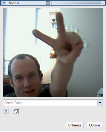 A small webcam video window showing a smiling man holding up two fingers in a V sign.