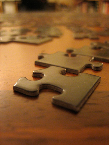 Close-up photograph of two jigsaw puzzle pieces about to be fitted together on a wooden table.
