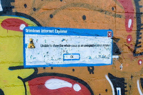 Photograph of graffiti-covered wall with a pasted-up image of an Internet Explorer error dialog.
